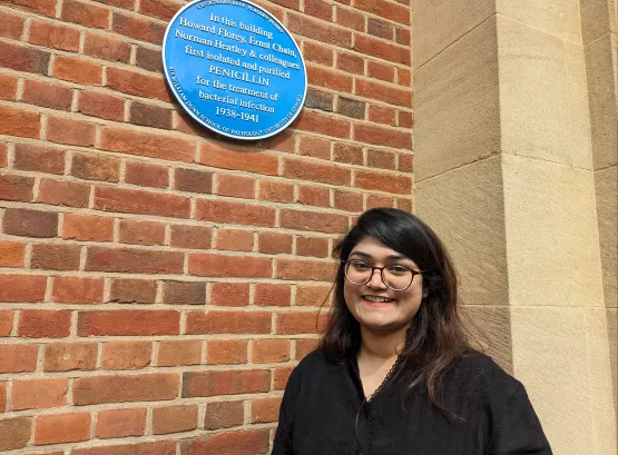 Dr Farhin Humayra in front of the blue plaque outside the Dunn School of Pathology