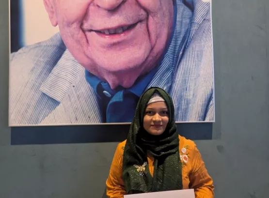 Sahanaz holding her certificate of attendance in front of a portrait of the Merieux foundation founder.