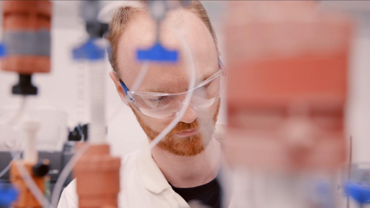 Liam working in the lab behind some equipment and tubes out of focus