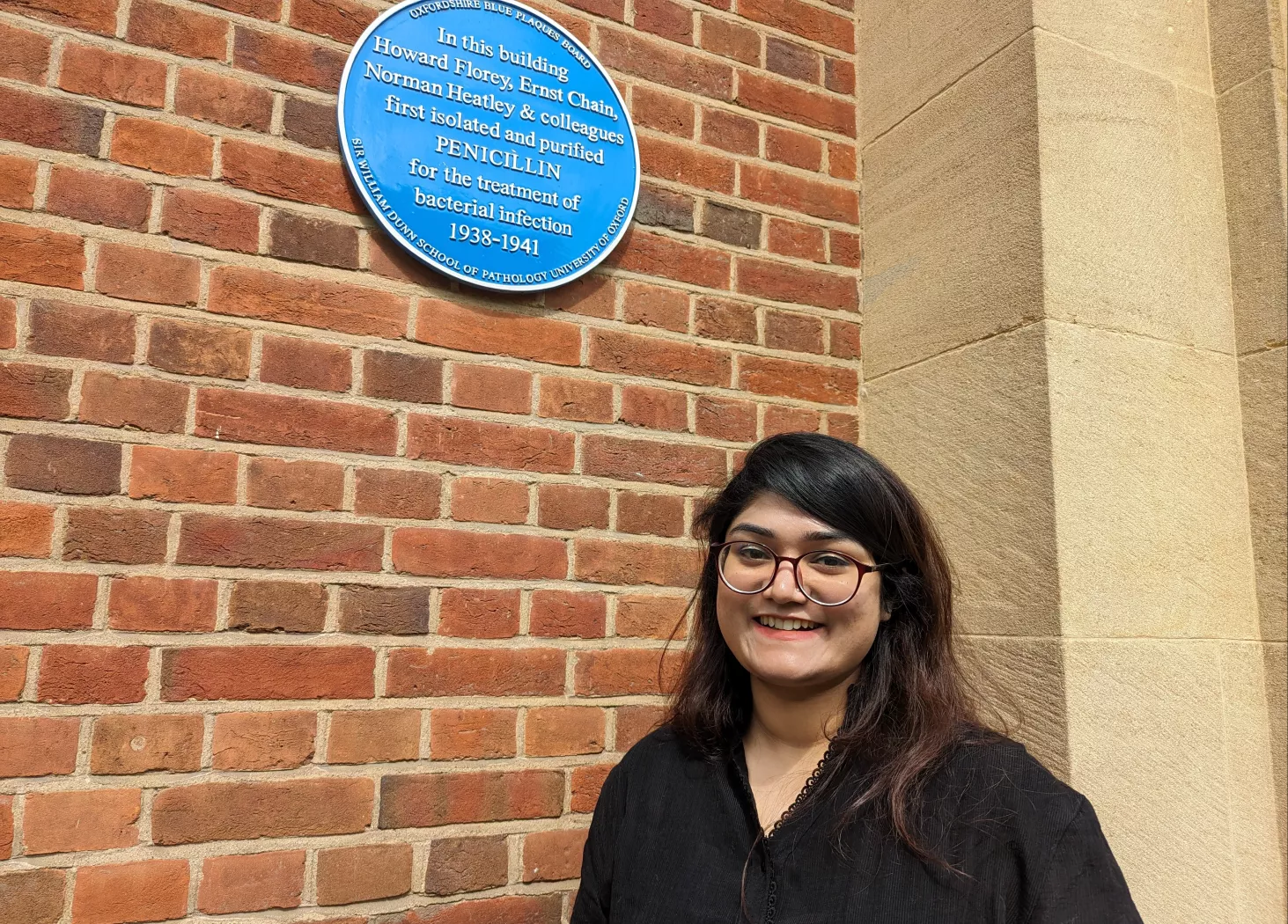 Dr Farhin Humayra in front of the blue plaque outside the Dunn School of Pathology